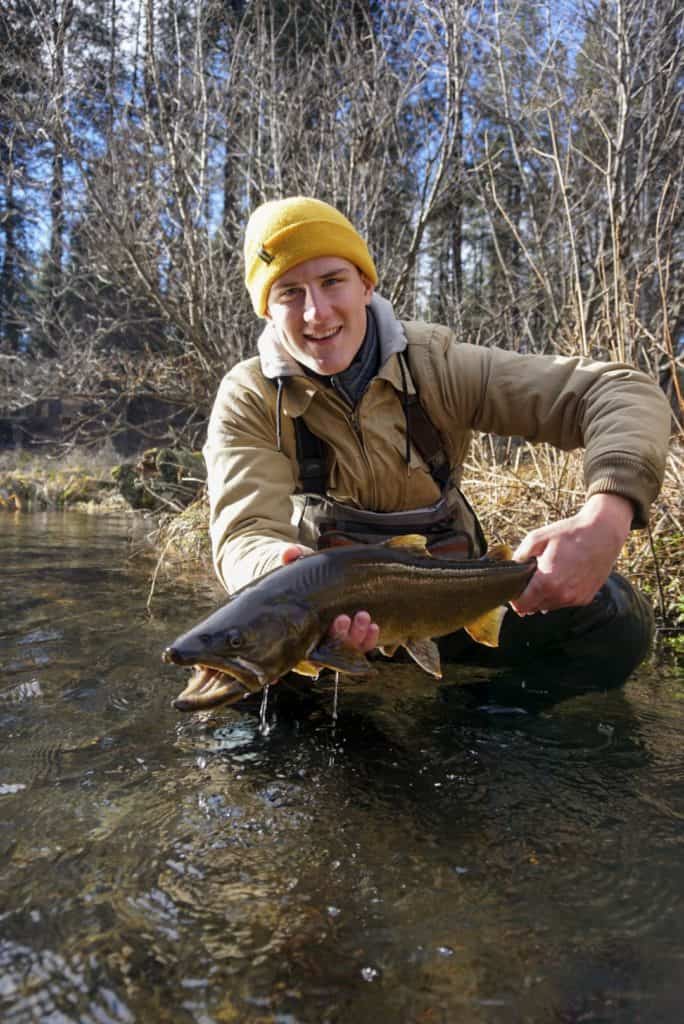 An angler holding a trout while crouching.