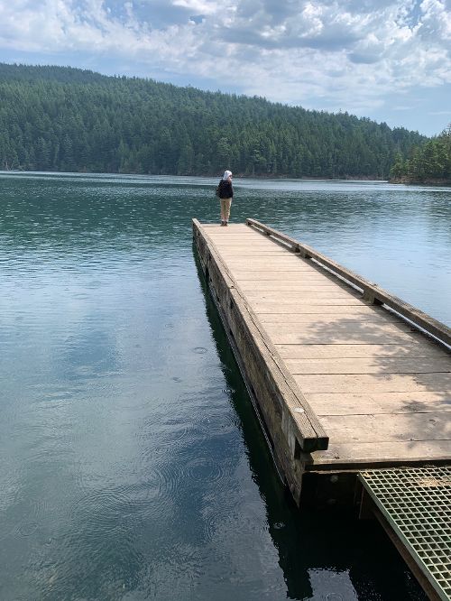 A woman standing on a pier at mountain lake in moran state park.